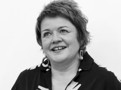 Kath has short cropped hair, a big smile and wears a black top.