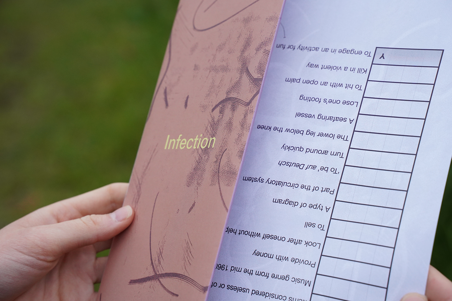 Hands holding a copy of the Infection publication. The background is a meadow.